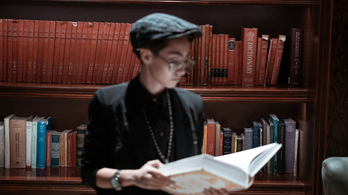 Person reading a book in front of a bookshelf filled with red leather-bound volumes in a stylish library.