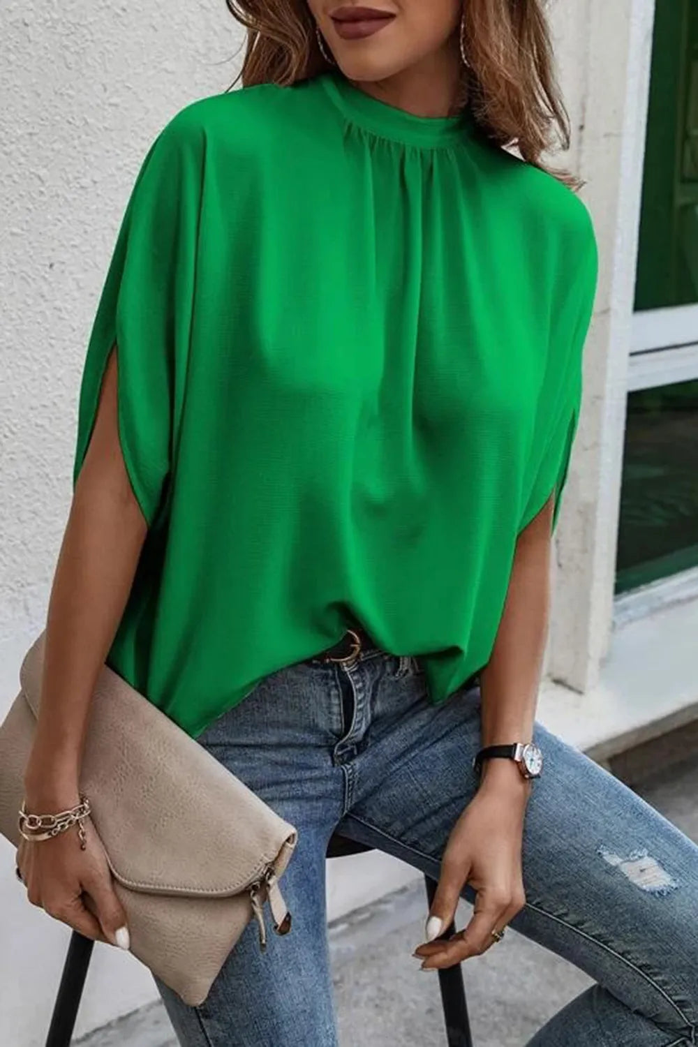 Stylish woman wearing a vibrant green tie back slit blouse, paired with jeans and a clutch bag.