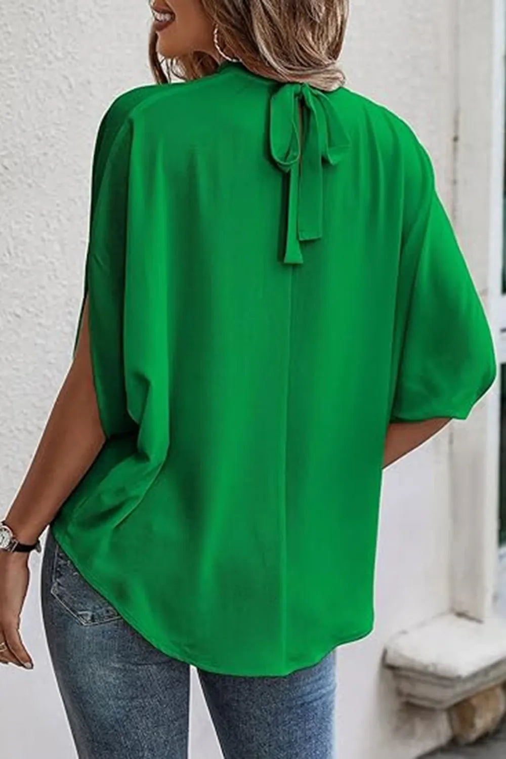 Back view of a woman wearing a green tie back slit blouse with a bow detail on the neckline.