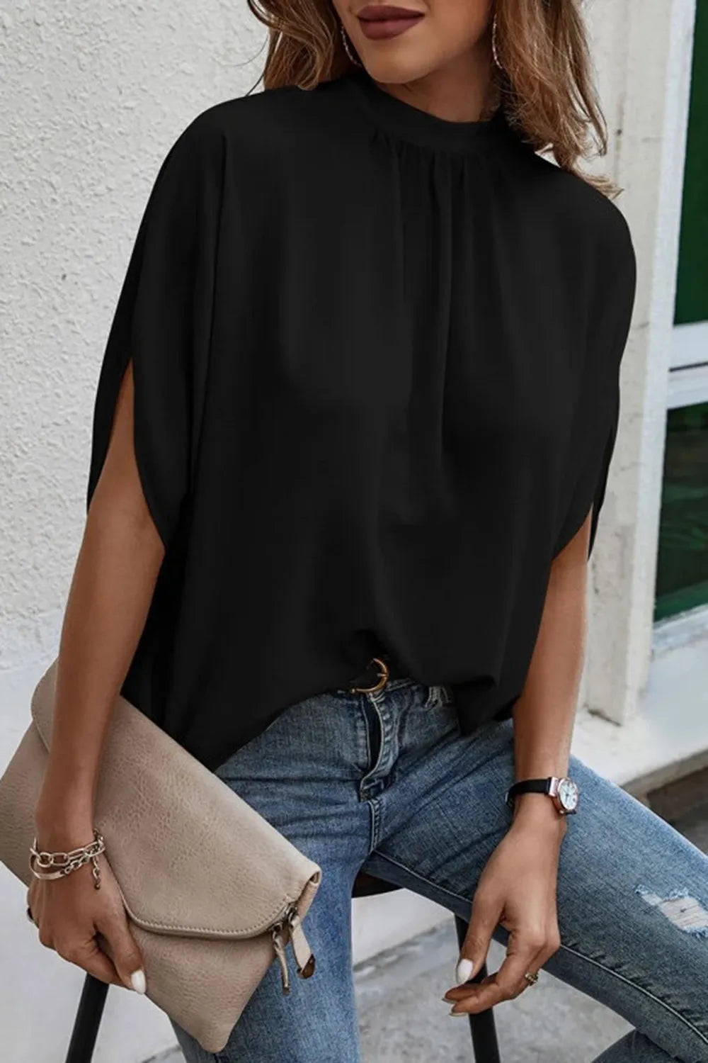 Model wearing a black tie back slit blouse with half sleeves, paired with jeans and a clutch bag.