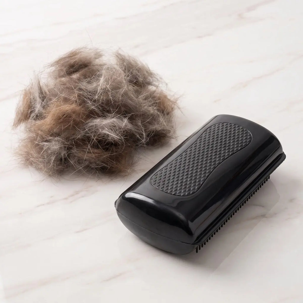 Dual-sided pet grooming comb for large animals beside a pile of loose hair on a marble surface.