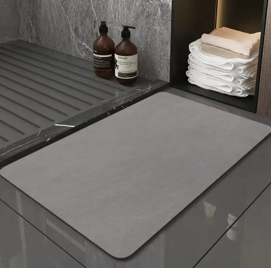 Modern diatom bathroom mat on a bathroom floor next to towels and toiletries.