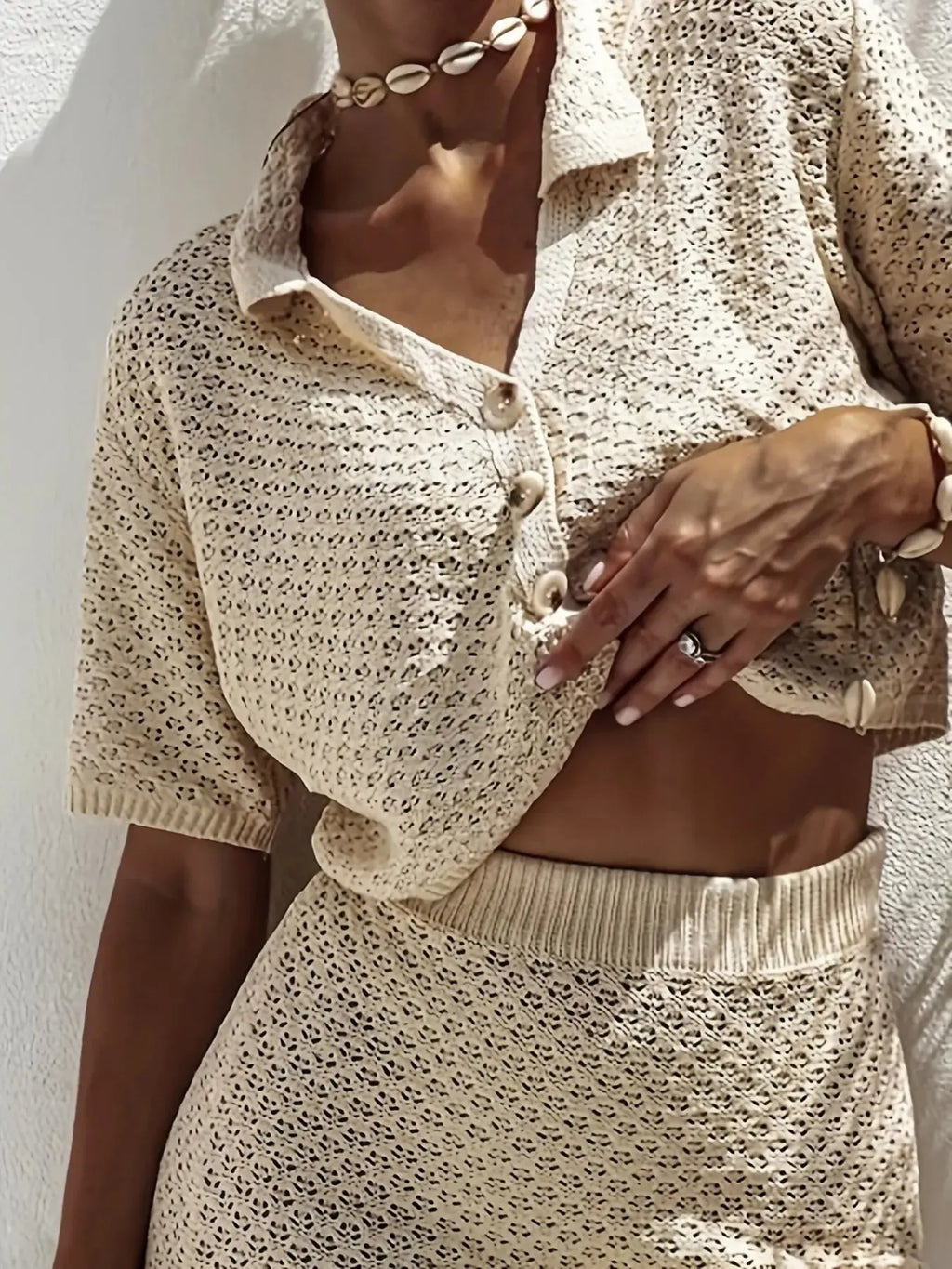 Close-up of a model wearing an openwork sweater set for women featuring a buttoned cropped top and matching skirt.