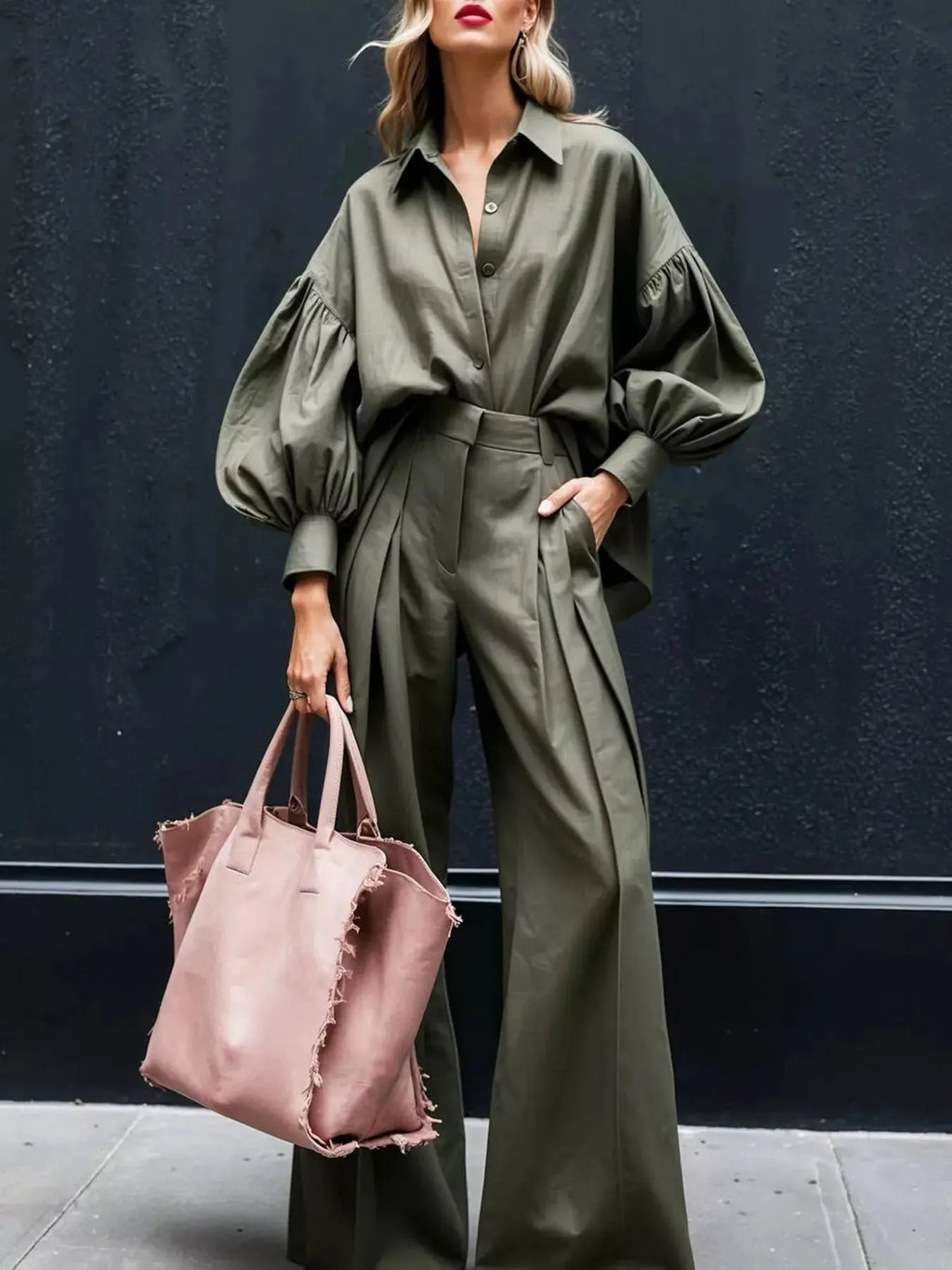Stylish model wearing a lantern sleeve shirt and wide leg pants set, holding a pink tote bag against a dark backdrop.